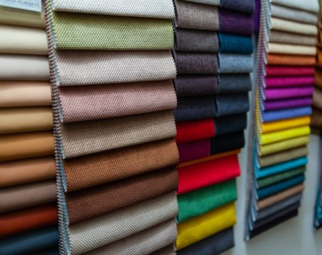 Pieces of textile material for interior trim and furniture making for example in the catalog of different colors for the design studio. Many colored materials hanging on the wall in stock.